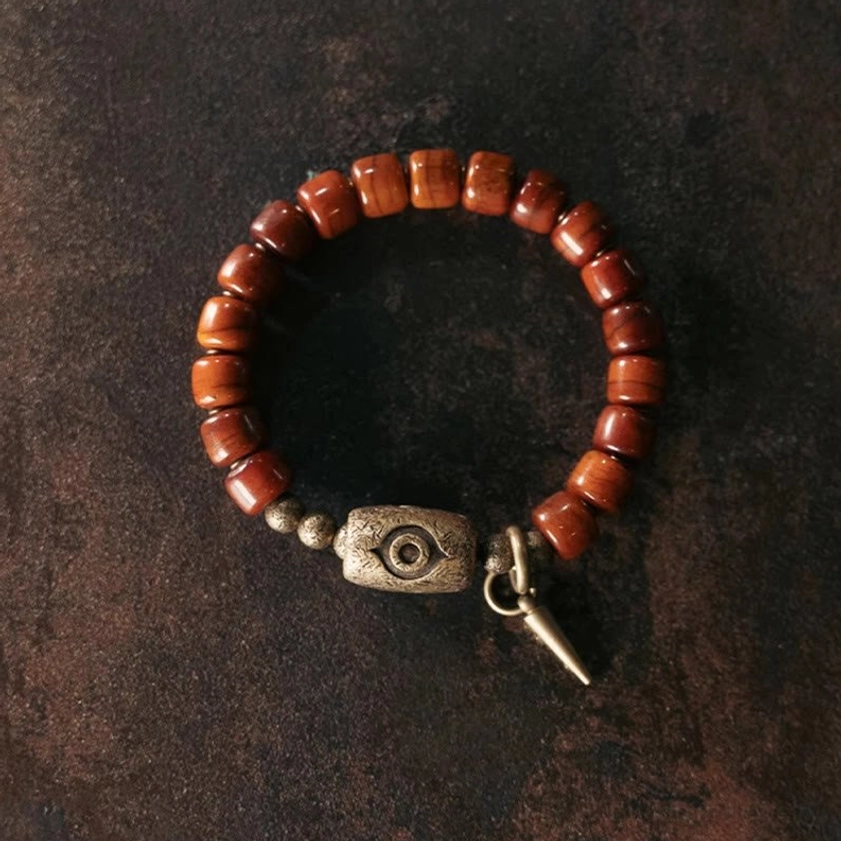 Circular overhead view of bone beads Buddhist protection bracelet with polished wooden beads and antique bronze Dzi charm
