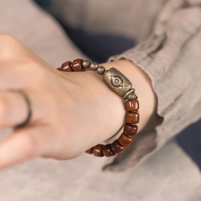 Hand-worn bone beads Dzi eye bracelet on wrist with copper cone pendant and natural wood grain detail close-up