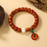 Bone beads Lotus and Peace Buckle bracelet with red charm flat lay on wooden surface