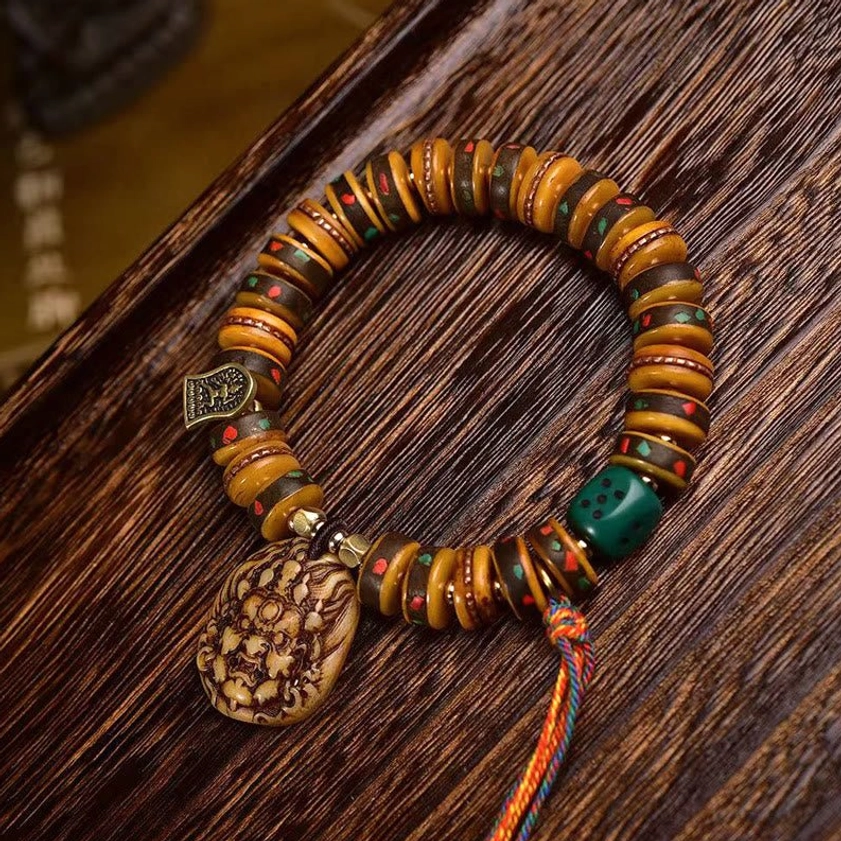 Top view of carved bone Buddhist bracelet displaying flat bead strand, spiritual deity pendant, copper charm, and vibrant ritual tassel
