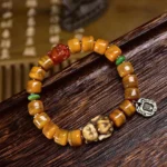 Handcrafted bone bead bracelet with red dzi stone and carved fox charm, overhead view on dark wooden tray