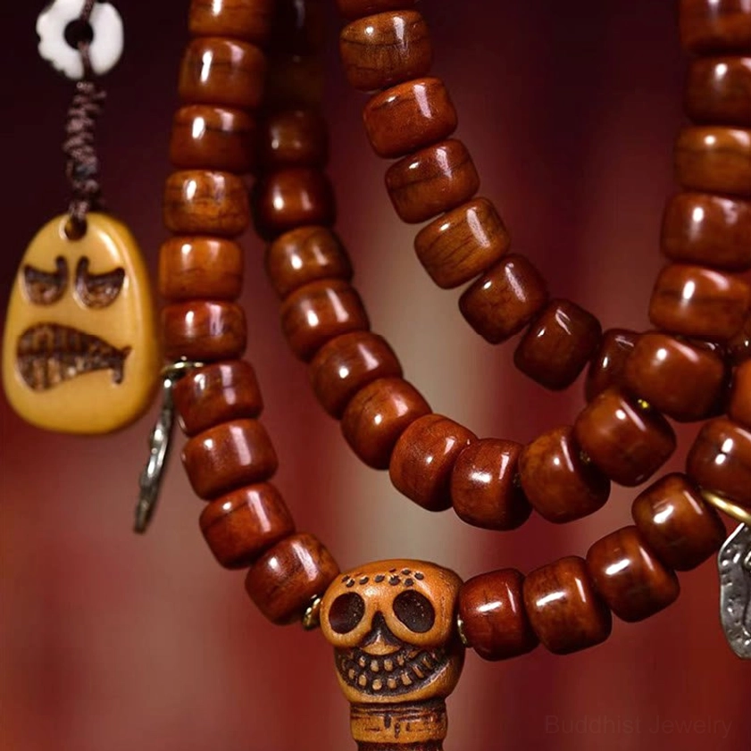 Detailed close-up of bone bead mala with hand-painted Dzi amulet, skull guru bead, grimace pendant and silver metal accents on red background