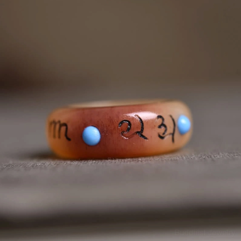 Camel bone mantra ring close-up - horizontal flat view of two-tone color scheme with engraved mantras and dual blue inlay beads