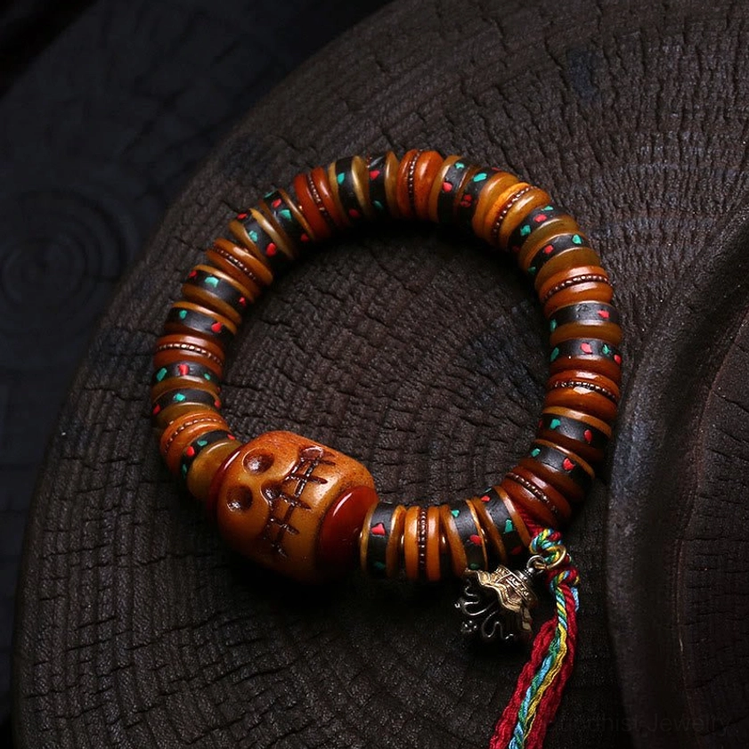 Tibetan bone skull bead bracelet with carved skull bead and multicolor tassel on wooden tray