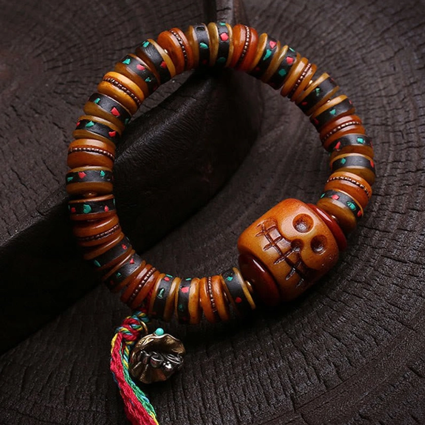 Angled top-down view of handmade bone skull bead bracelet with multicolor tassel and metal charm