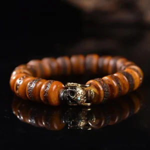 Vintage bone skull bracelet with copper ornament – overhead view showing aged brown bone beads and metal charm on black reflective surface