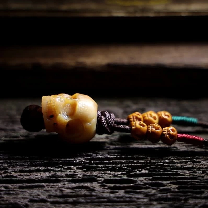 Bone skull pendant with decorative beads and colored cord lying flat on dark wooden surface