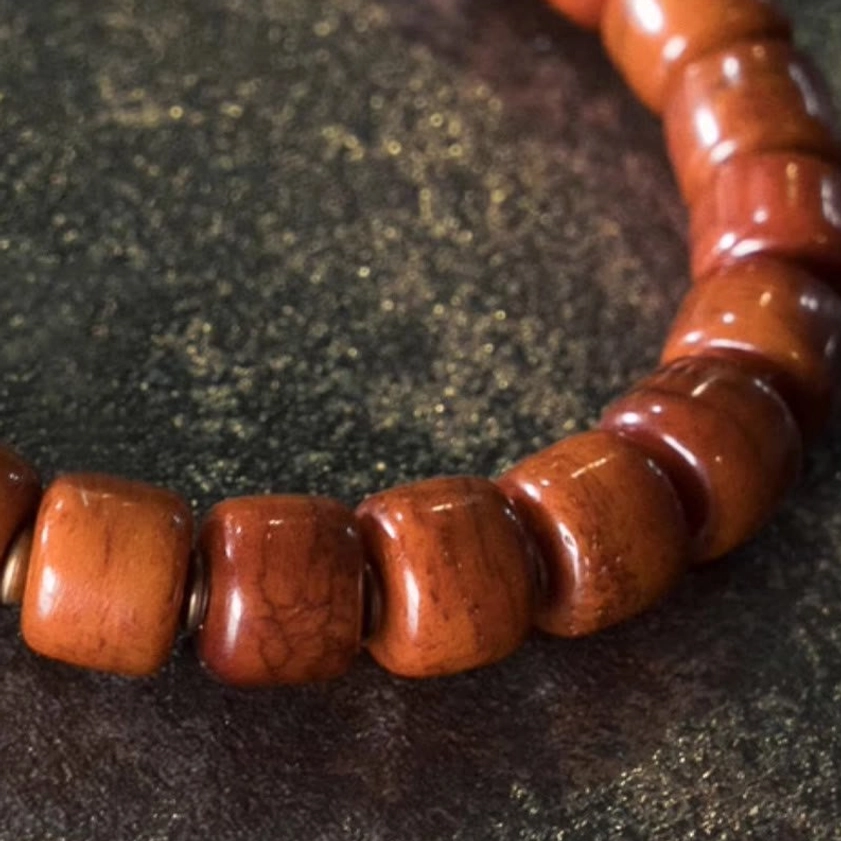 Extreme close-up of beaded strand showing matte reddish-brown cylindrical beads with natural grain texture and antique metal spacer beads