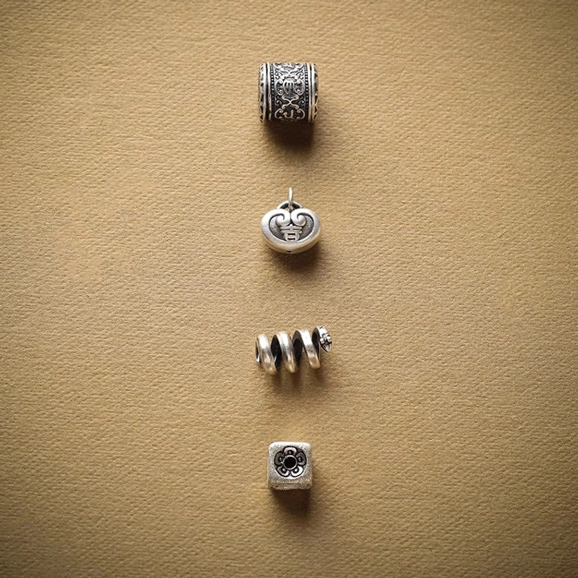 Buddhist bracelet charm components including carved bead, lock charm, spiral adjuster, and square pendant