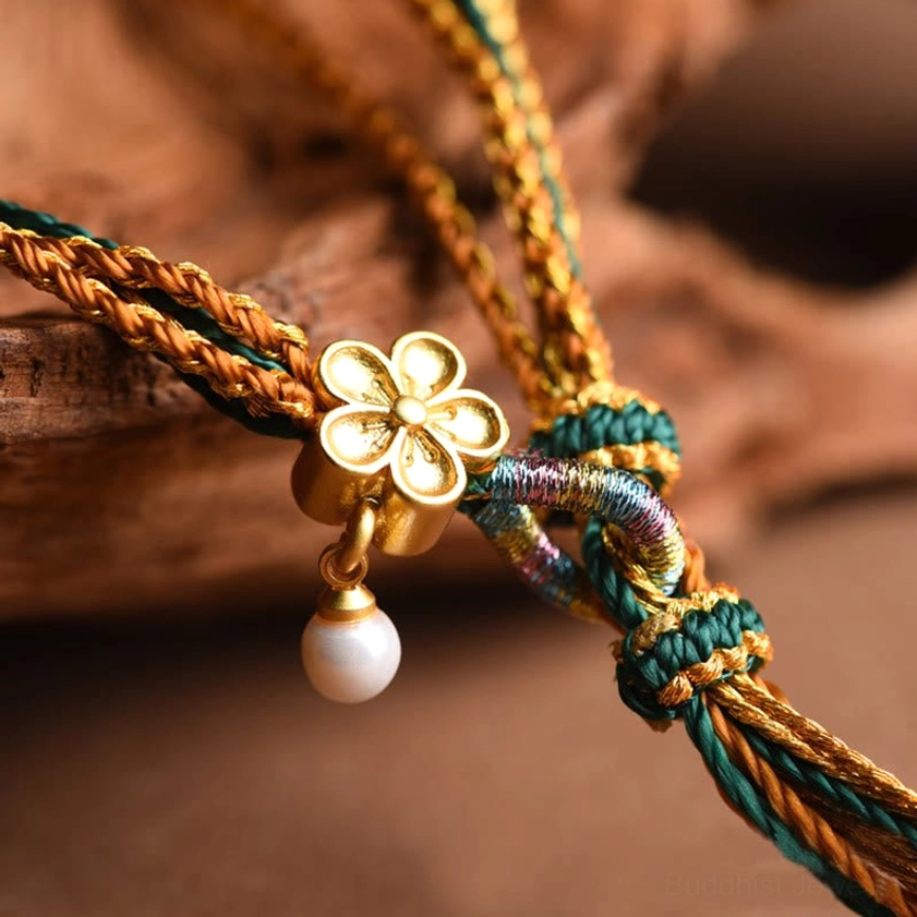 Handmade braided bracelet charm detail showing gold four-leaf clover, white pearl pendant, and mixed woven cord texture