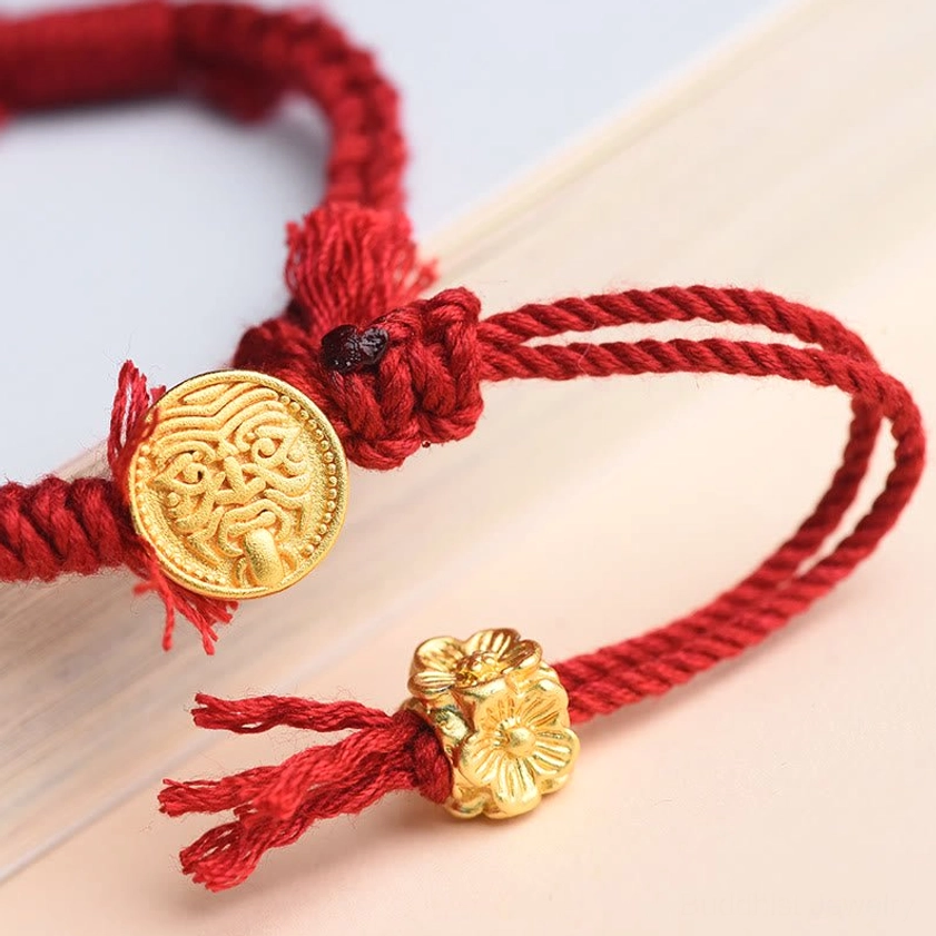 Close-up detail of red string bracelet showing gold flower clasp, engraved disc, and hand-braided red cord craftsmanship