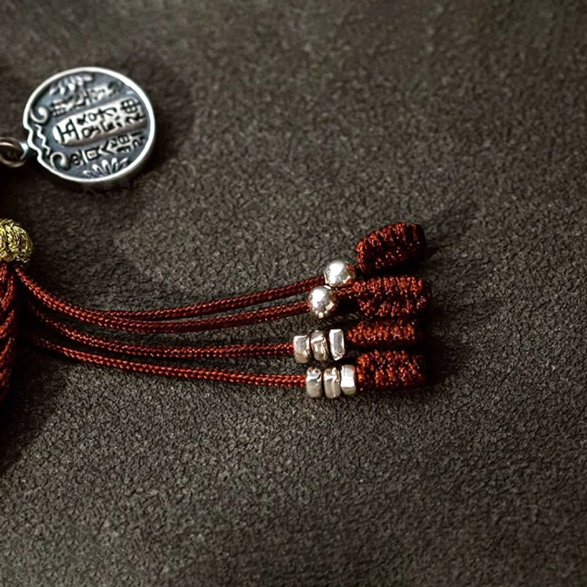 Flat lay of Buddhist bracelet components showing five wealth gods pendant, red protective cord, and silver spacer beads