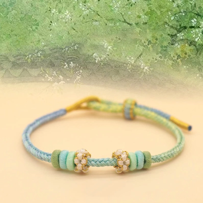 Gradient blue-green-yellow Buddhist string bracelet with peach blossom ornament on spring scenery background