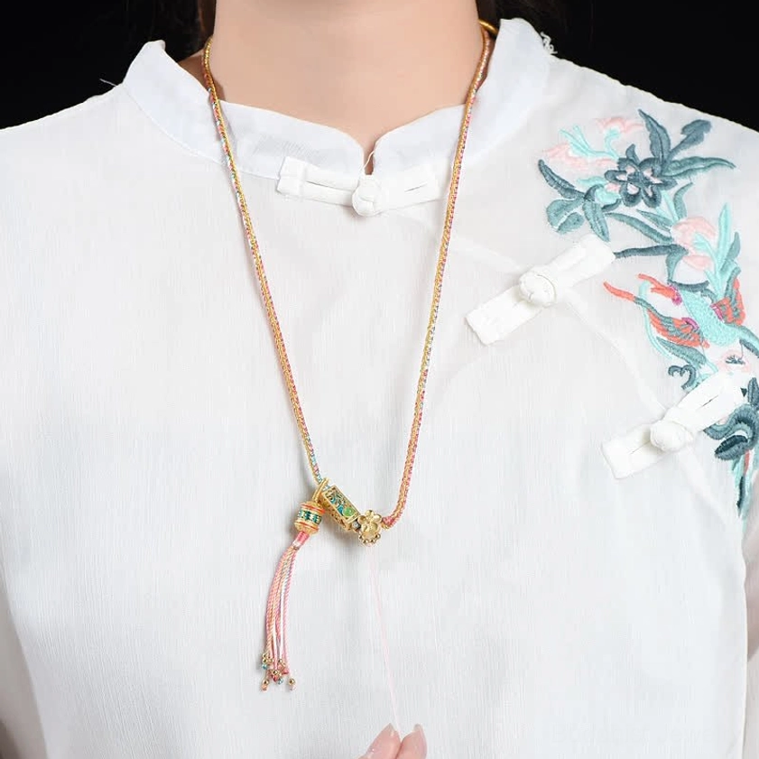 Tan and pink braided copper Buddhist necklace worn on white embroidered shirt, showing close-up of enamel pendant charm