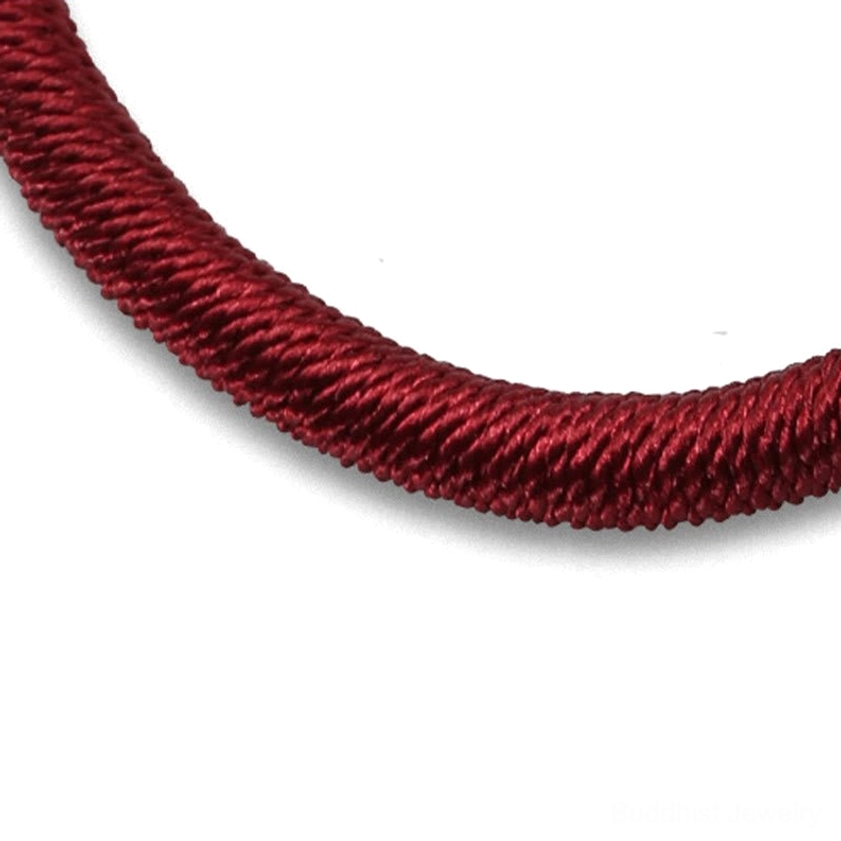 Macro close-up of braided Buddhist bracelet cord showing burgundy twisted woven texture and tight braided structure on white background