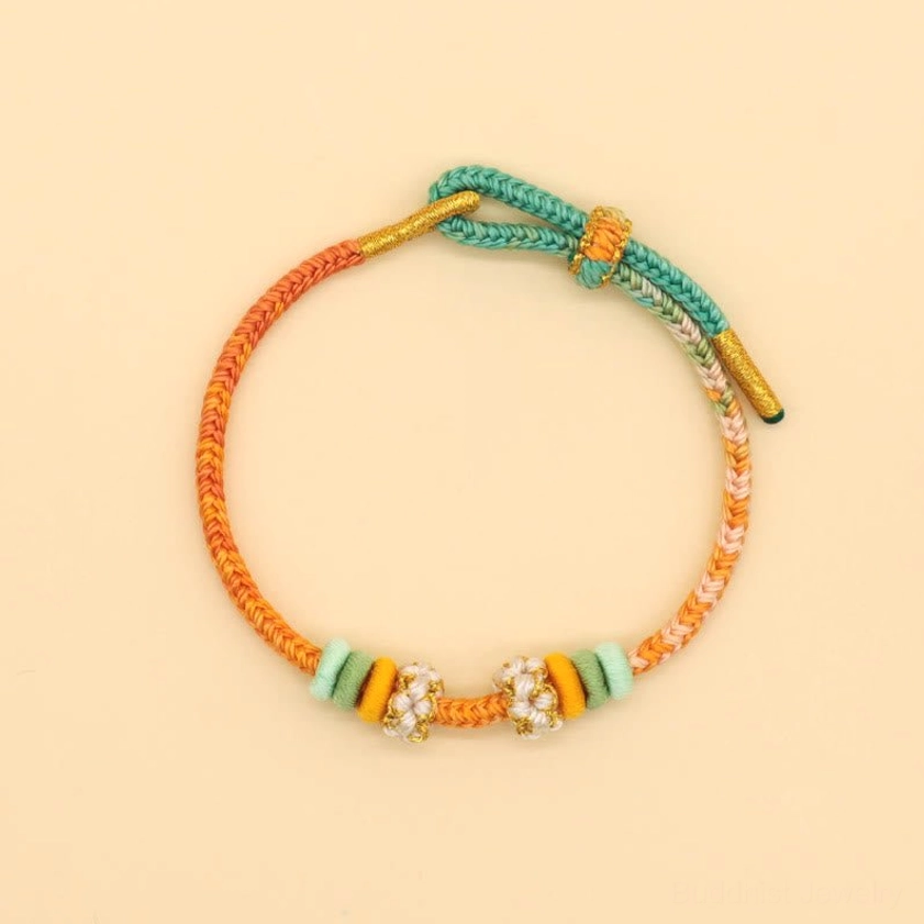 Artisan Buddhist braided bracelet featuring orange, teal, and gold tones with flower bead charm