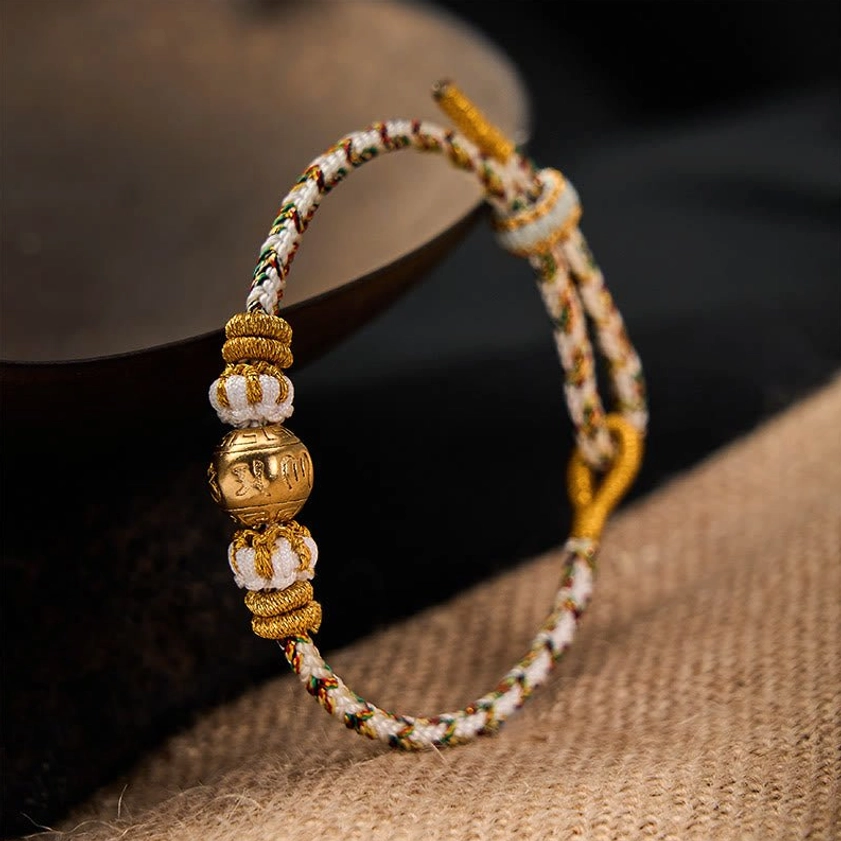 Close-up side view of white braided spiritual bracelet with carved gold-toned engraved bead and woven rope details