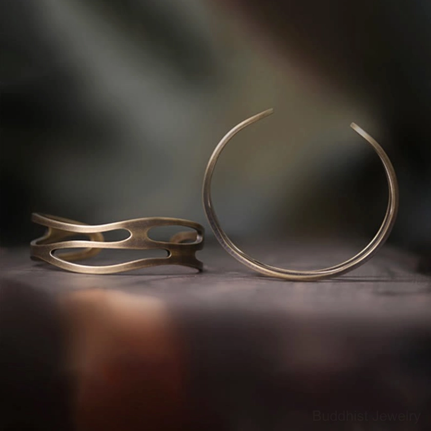 Two styles of brass Buddhist bangles flat lay comparison showing hollow cuff bracelet and simple open hoop design in antique bronze