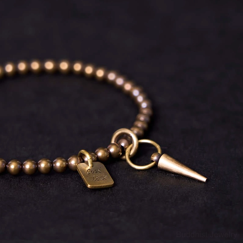 Tight close-up of antique brass beaded bracelet showing tightly arranged beads with engraved Good Luck tag and spike pendant