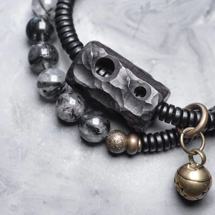 Buddhist protection bracelet side angle close-up showing hanging brass bell and carved ebony wood charm detail
