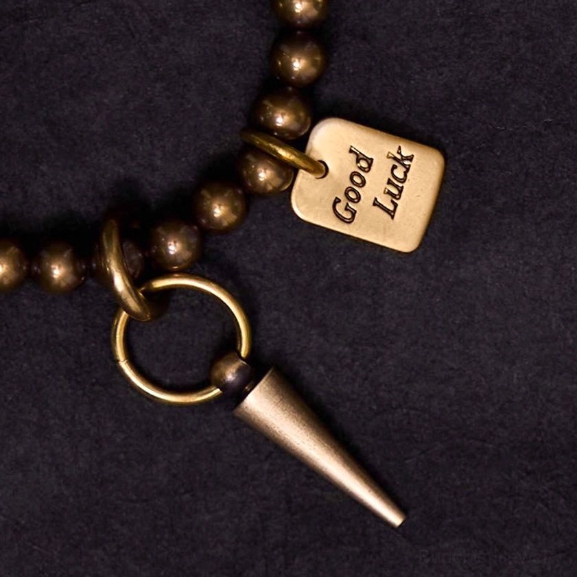 Close-up macro shot of brass beaded bracelet showing engraved Good Luck metal tag and spike charm detail