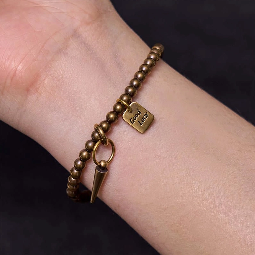 Wrist close-up of vintage brass beaded bracelet on bare skin showing antique finish and Good Luck charm