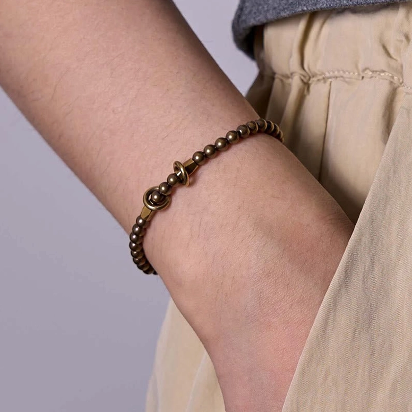 Women's lifestyle photo of brass couple bracelet worn on female wrist with linen casual wear and compact toggle clasp