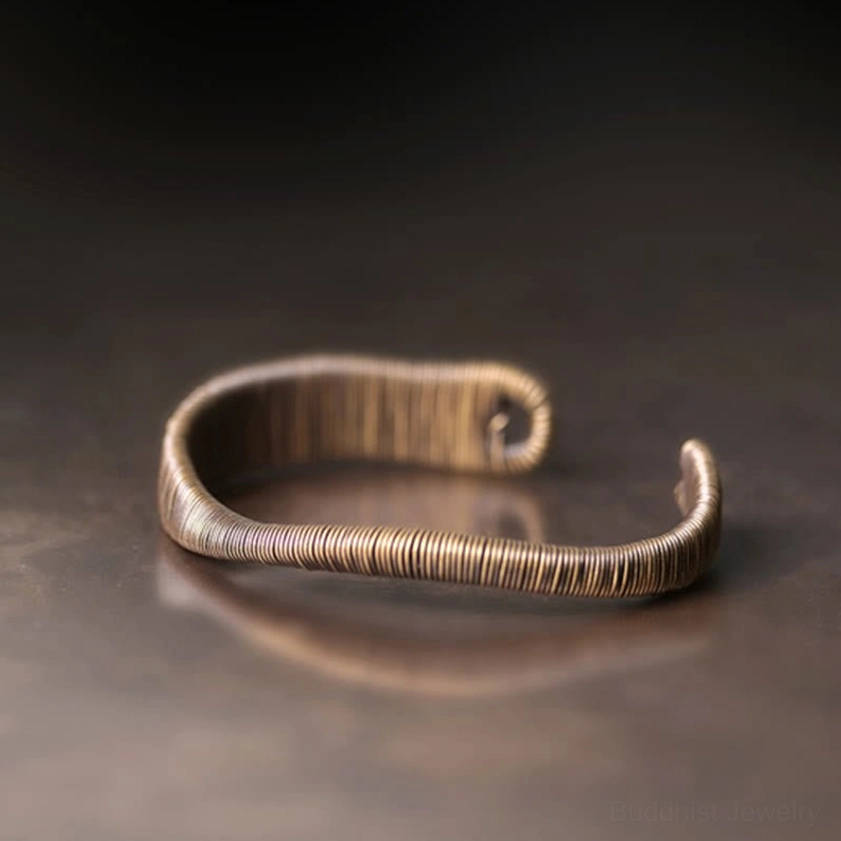 Buddhist brass cuff bracelet front high-angle view featuring coiled wire texture and curved open ends