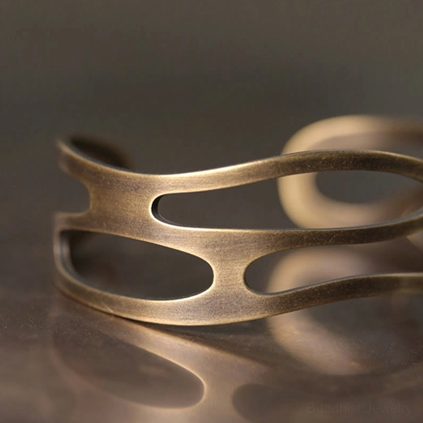 Close-up side view of brass prosperity bracelet showing curved hollow design and vintage metal finish on reflective wooden surface