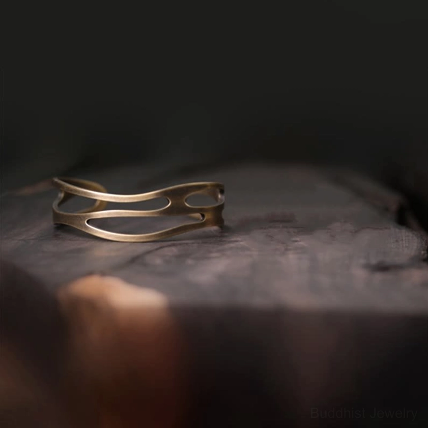Slim hollow brass prosperity cuff bracelet oblique side view on dark wood table showing minimalist streamline design and antique metal finish