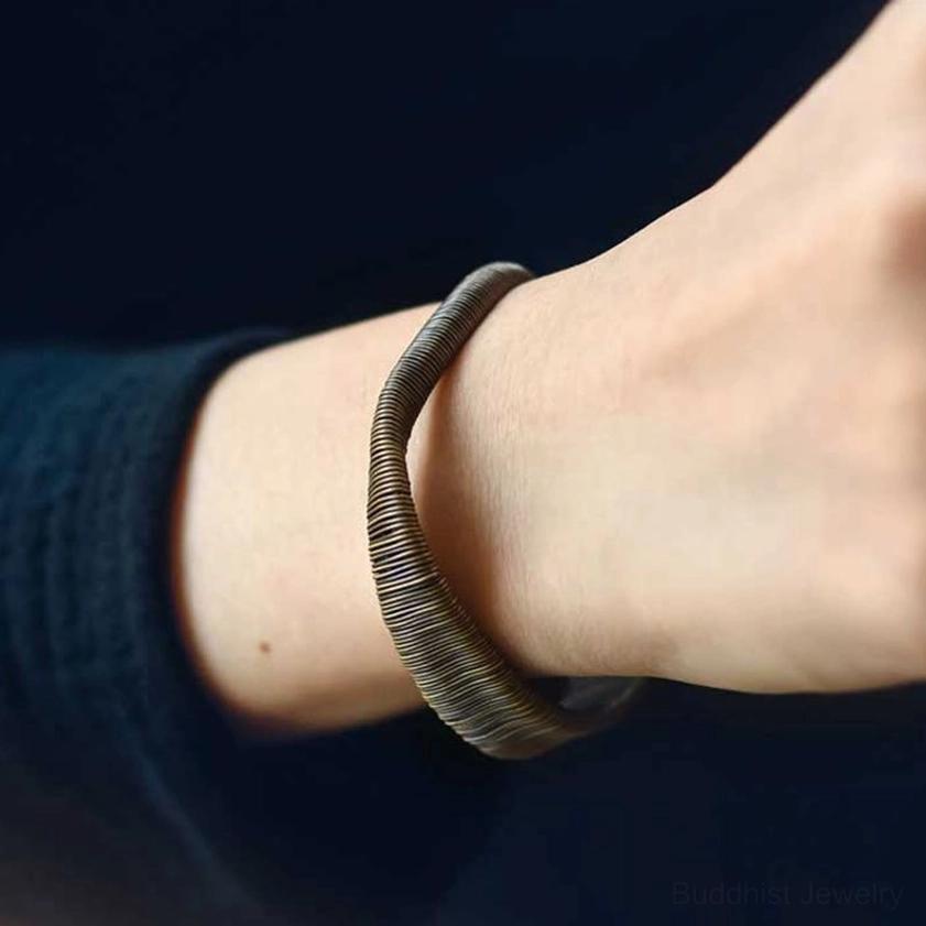 Brass wrapped cuff bracelet worn on human wrist showing dark grey-bronze tone and how the adjustable bracelet fits on skin