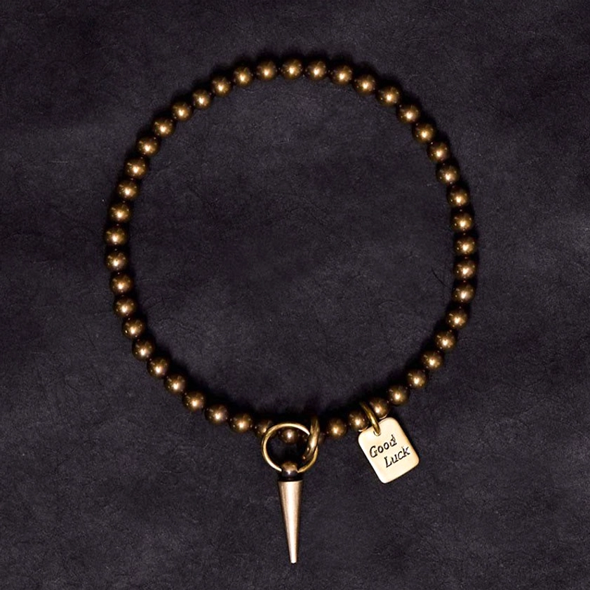 Circular brass Buddhist bracelet with engraved Good Luck tag and spike charm - flat lay top-down perspective