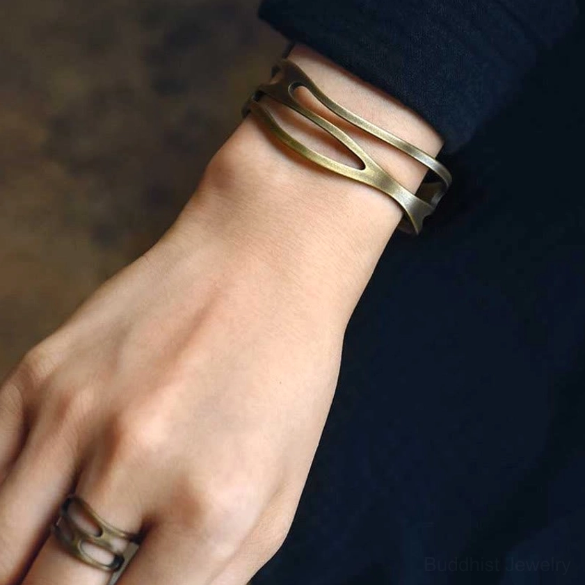 Brass prosperity cuff bracelet worn on wrist showing comfortable fit and slim multi-band hollow design against dark clothing