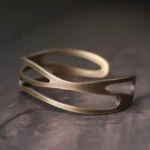 Vintage brass prosperity cuff bracelet with curved hollow design on dark wood surface, showing intricate multi-layer metalwork and warm antique bronze finish