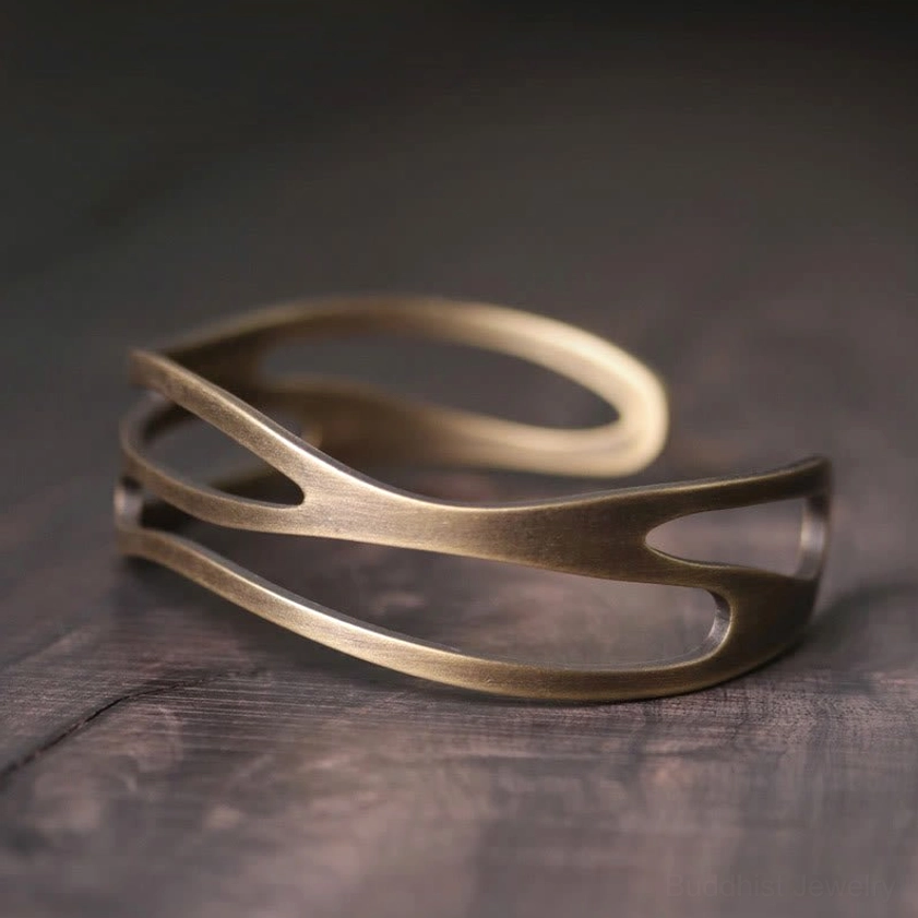 Vintage brass prosperity cuff bracelet with curved hollow design on dark wood surface, showing intricate multi-layer metalwork and warm antique bronze finish