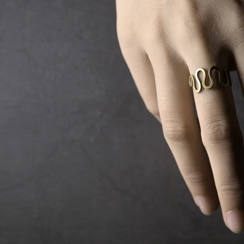Woman wearing curved brass prosperity ring on middle finger close-up front view displaying sleek wavy design