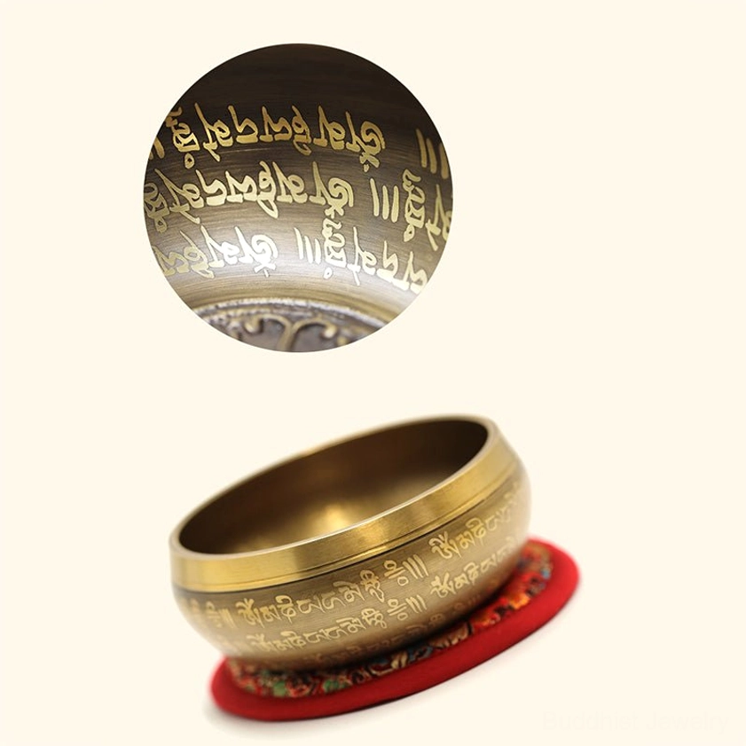 Handcrafted brass singing bowl positioned on red embroidered cushion showing engraved inner scriptures and detailed surface patterns