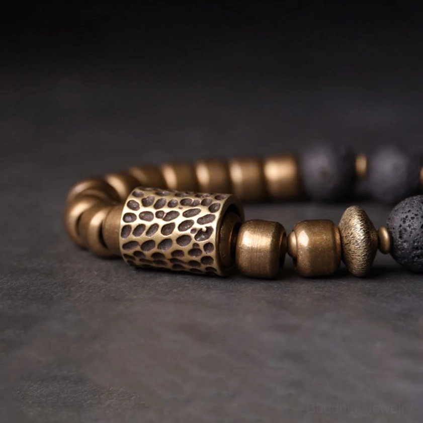 Detailed side view of engraved brass spacer bead with adjacent lava rock beads, showing intricate craftsmanship and texture
