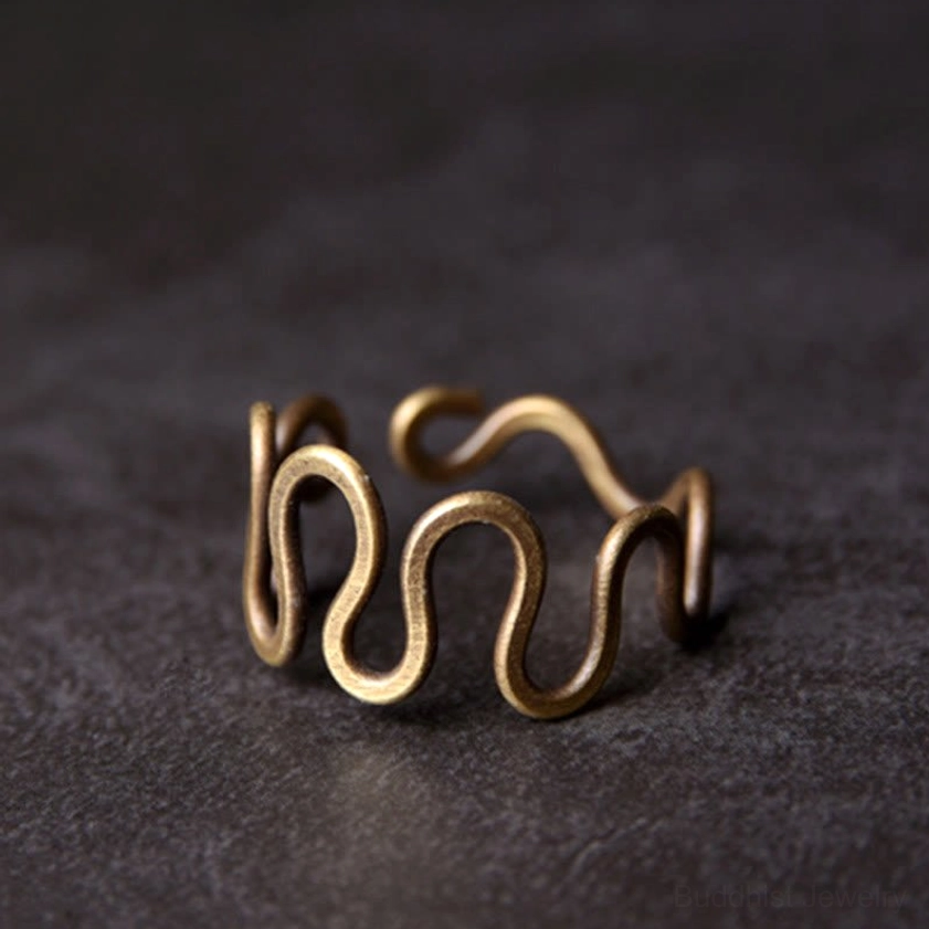 Hand wearing curved brass wave ring on multiple fingers showing antique golden bronze tone and flexible fit