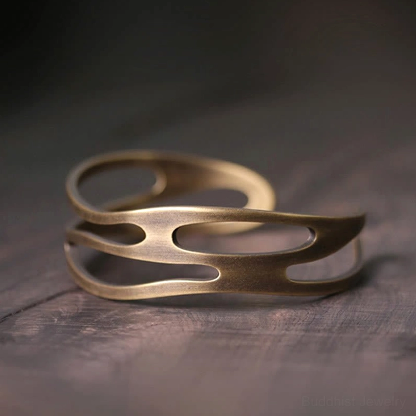 Handcrafted brass open cuff bracelet front three-quarter view displaying carved hollow cutout structure and brushed antique bronze patina