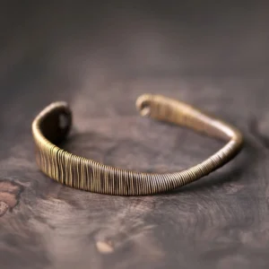 Brass wrapped open cuff bracelet with vertical wire winding detail, showing adjustable design from top-down angle on wooden surface