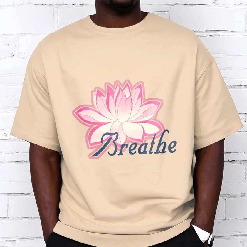 Man wearing breathe lotus flower beige tan t-shirt with pink lotus and cursive dark blue text on white brick wall