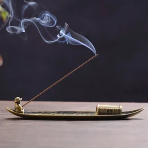 Bronze fishing boat incense holder with burning incense stick and fisherman figurine on wooden table