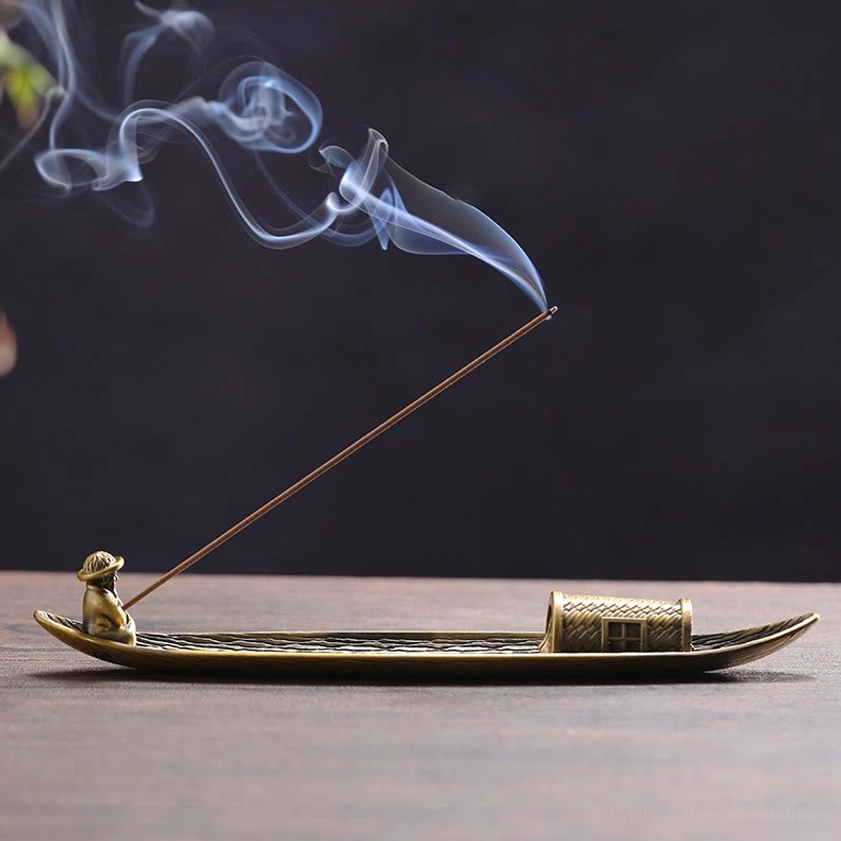 Bronze fishing boat incense holder with burning incense stick and fisherman figurine on wooden table