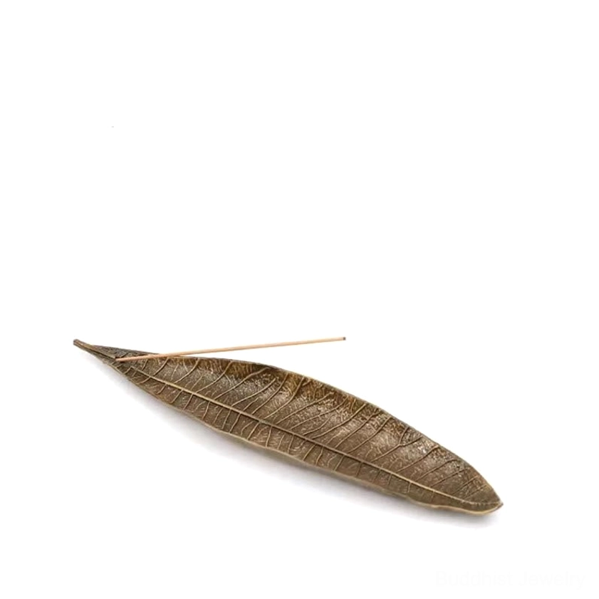Overhead flat lay of bronze alloy leaf incense holder on white background holding single incense stick