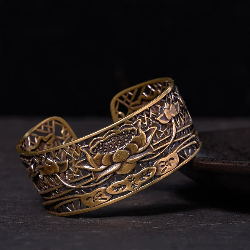 Bronze-tone hollow lotus open cuff bracelet from low side angle on dark wooden table with ceramic plate, showing warm antique finish