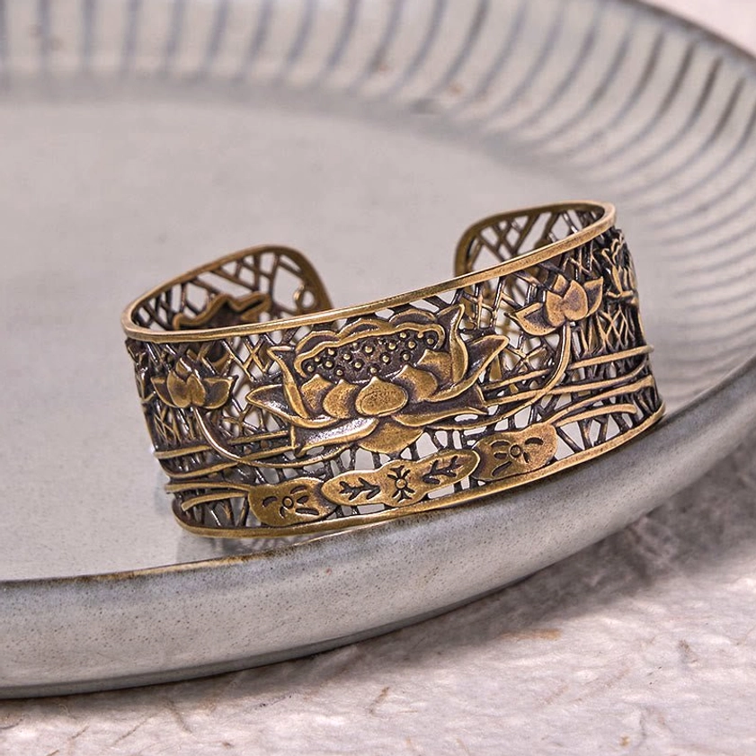 Bronze-tone lotus cuff bracelet three-quarter angle on light grey ceramic serving tray, displaying detailed hollowed floral relief design