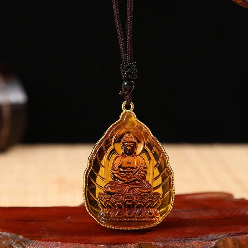 Brown Buddhist Buddha crystal pendant with gold metal frame and black beaded wax cord, front view showing seated Buddha engraving on red wooden display base