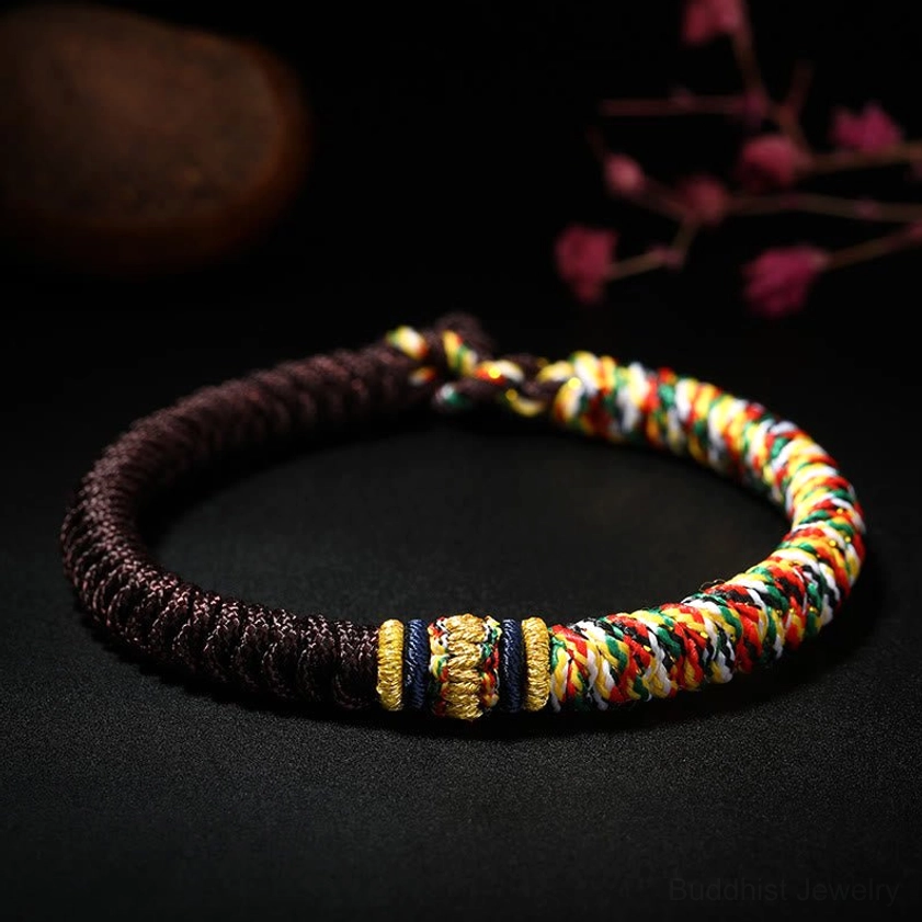 Brown handmade Buddhist King Kong Knot bracelet with multicolored accent threads and traditional braiding pattern on dark backdrop