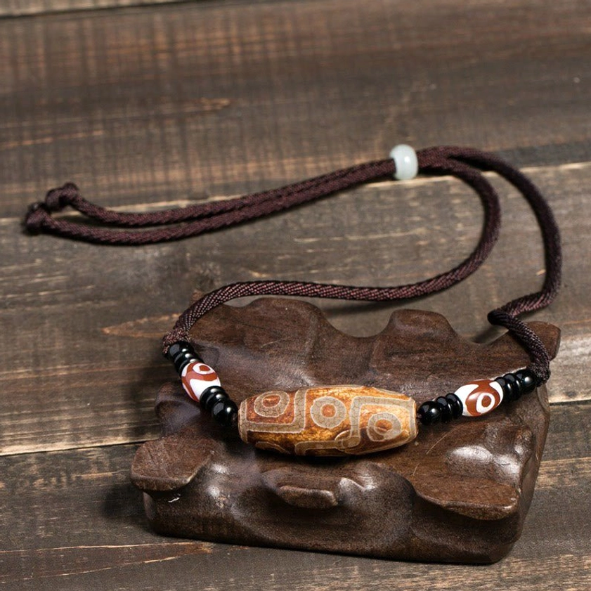 Carved brown Buddhist dzi bead necklace with adjustable braided cord and three-eye decorative beads, oblique display angle